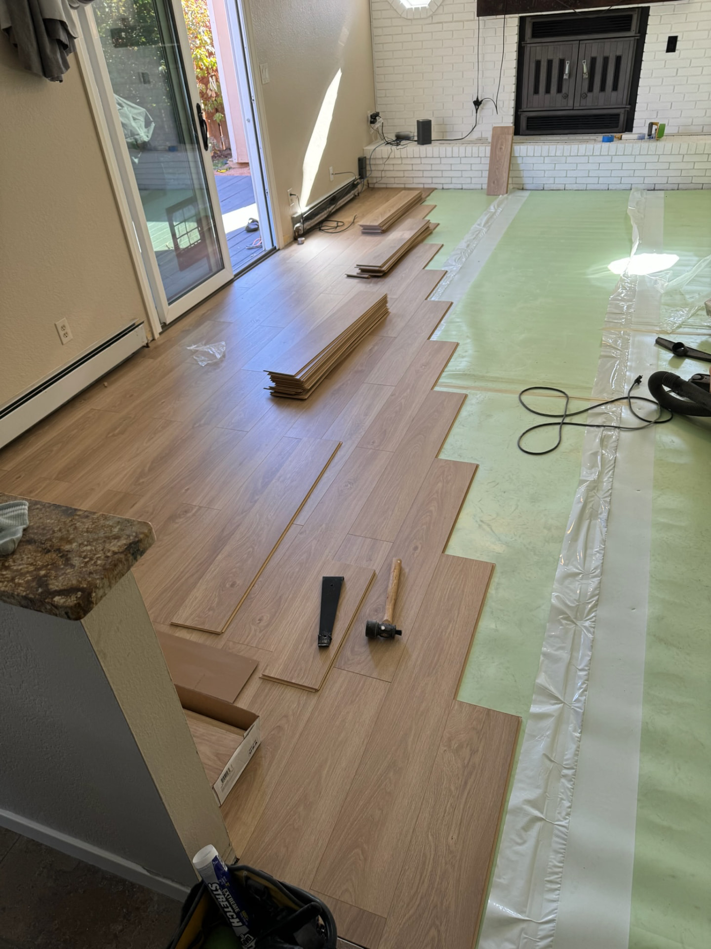 Laminate plank flooring being installed over green underlayment in a living room
